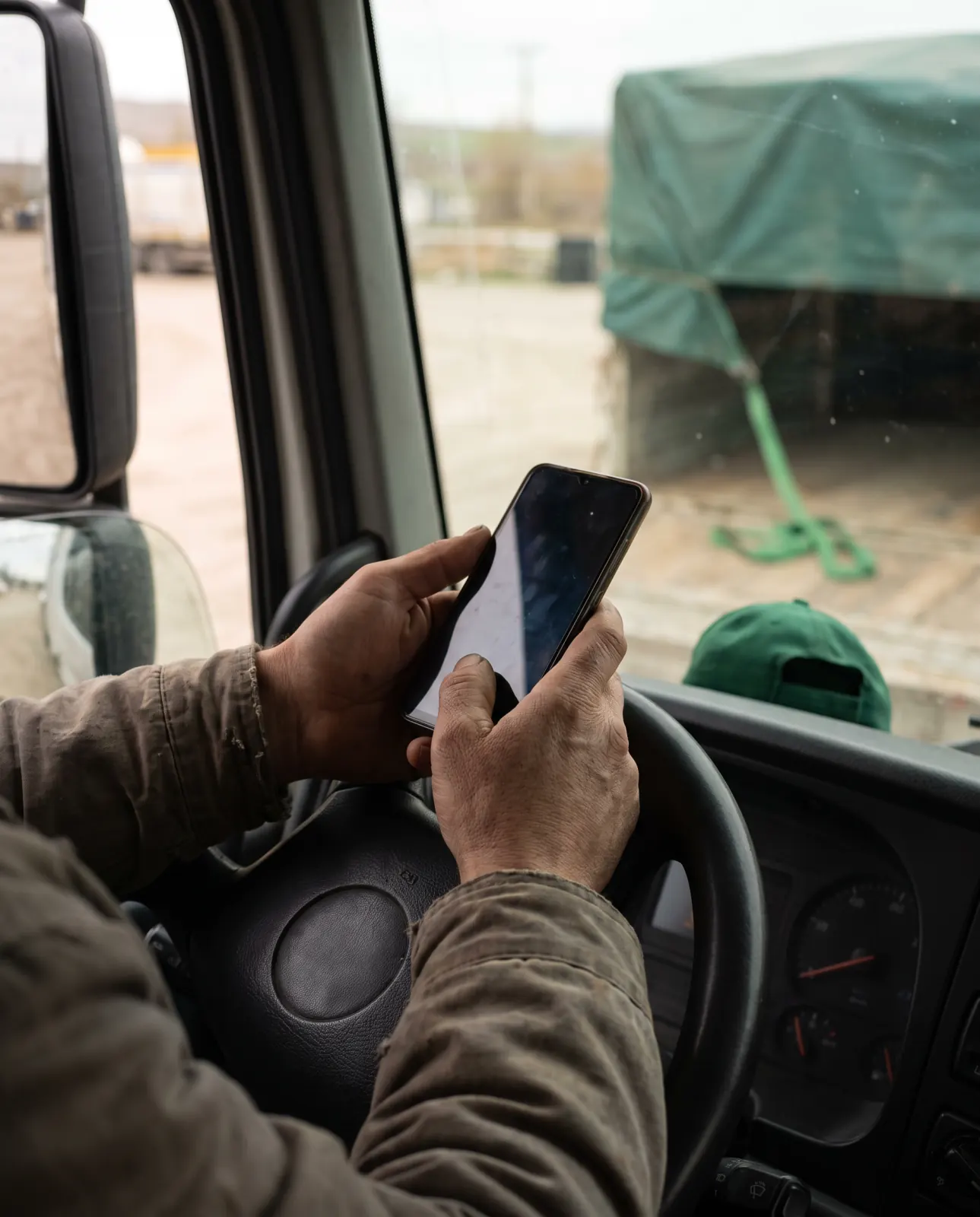 Sahada telefonu tutan eller; arkada kamyon kabini ve yükleme alanı bulanık görünüyor.