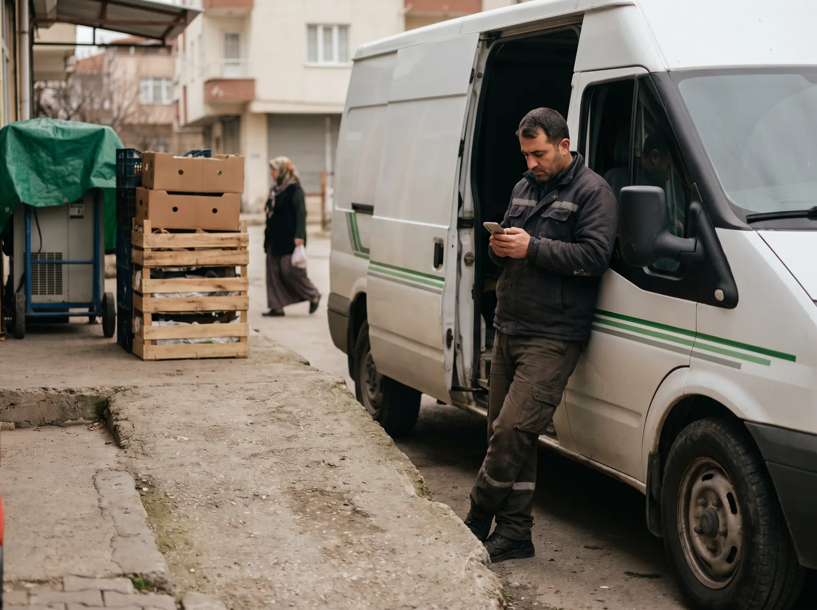 Yükleme rampasındaki dağıtım aracının yanında şoför telefondan teslimat listesine bakıyor